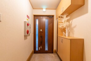 A hallway with a wooden door, a fire alarm, and a cabinet with a decorative item. - Ten-Cha House - Self-Check In Only (Osaka)