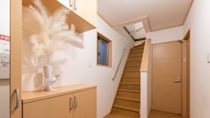A hallway with wooden flooring, a staircase, a door, and a cabinet with a decorative item. - Ten-Cha House - Self-Check In Only (Osaka)