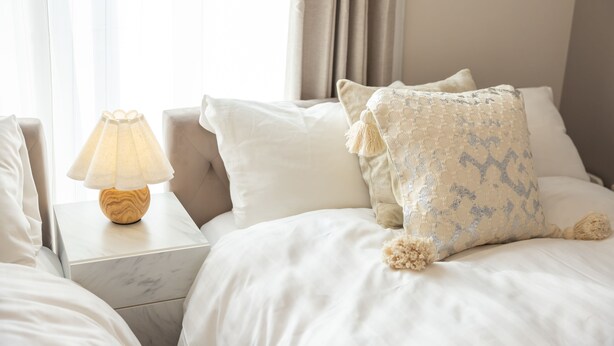 A neatly made bed with white linens, a wooden bedside table with a lamp, and a patterned throw pillow. - Ten-Cha House - Self-Check In Only (Osaka)