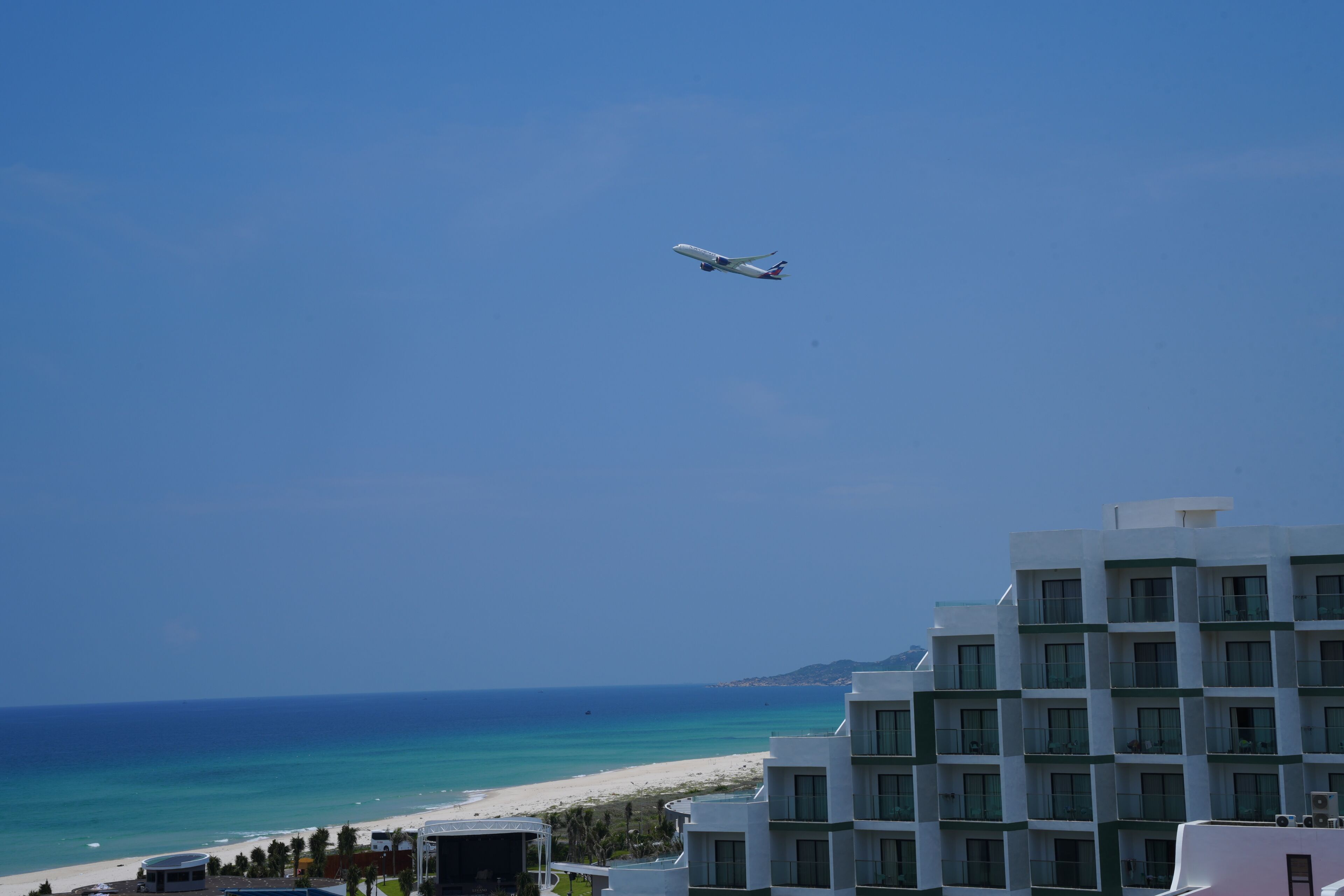 An airplane flying over a beach with a hotel in the foreground.