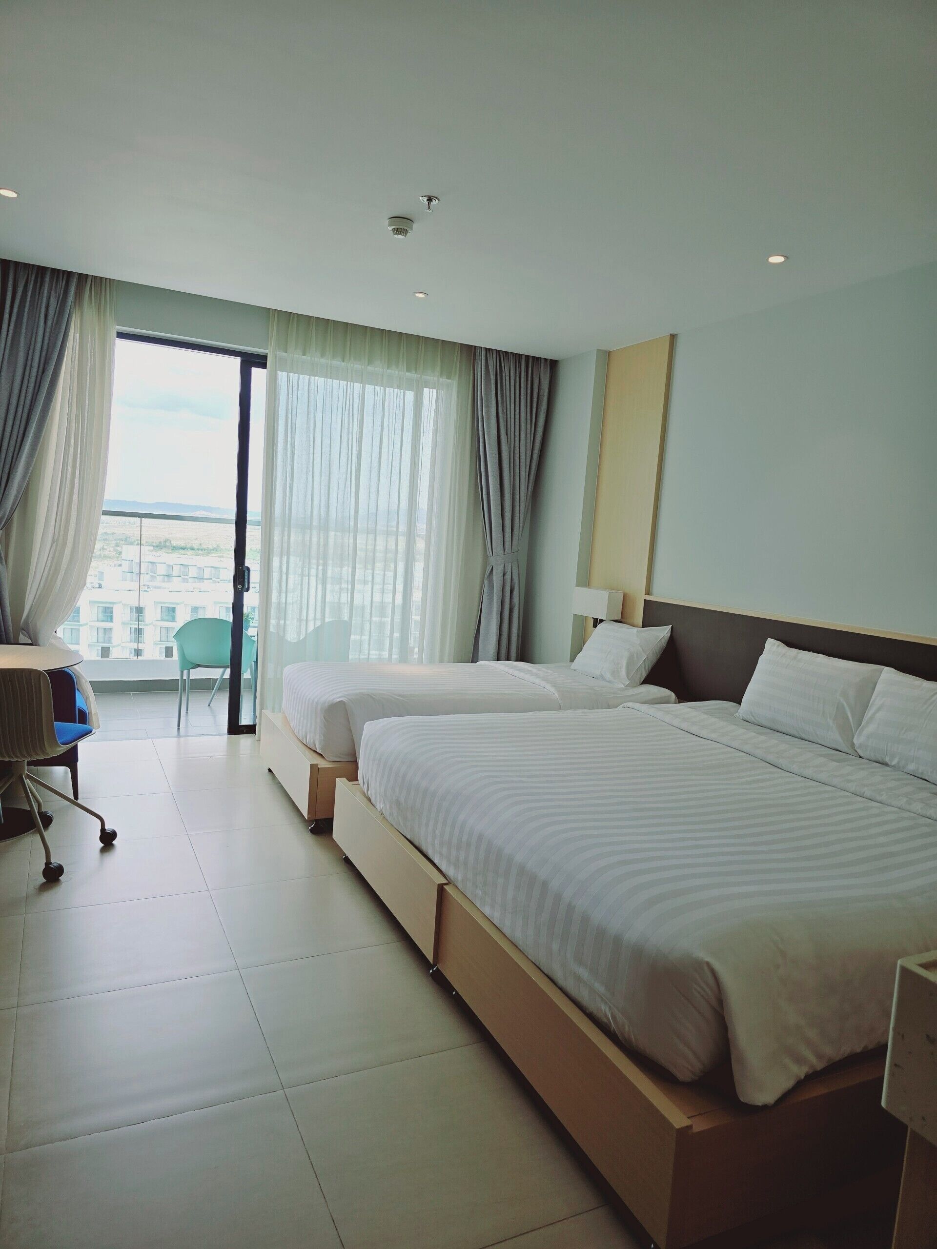 Ein Hotelzimmer mit zwei Betten, einem Schreibtisch, einem Stuhl und Blick auf die Stadt.