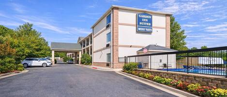 A Garden Inn Suites building with a clear sky, a parking lot, and a pool area with a fence.