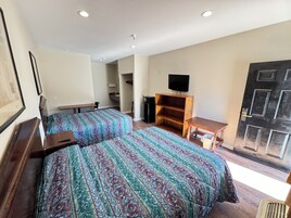 Una habitación con dos camas, televisión, escritorio de madera y una puerta.