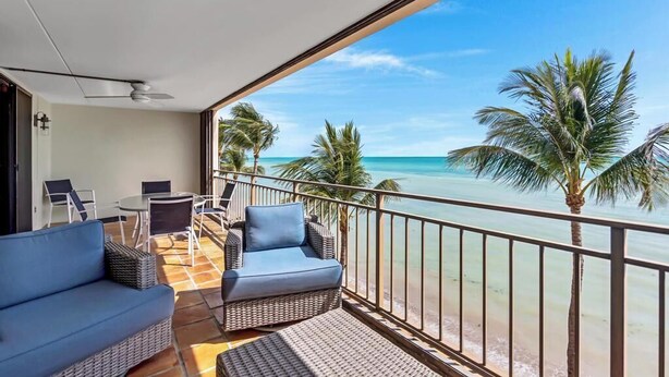 Un balcón con mobiliario de mimbre, vista a la playa y palmeras.