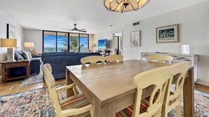 Un salón amplio con una gran mesa de madera para comer, un sofá y vista al océano a través de amplios ventanales.