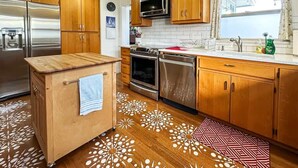 A kitchen with wooden cabinets, stainless steel appliances, a patterned floor, and a window with curtains. - Top Floor Apartment, Workspace, Near Downtown, ONP (Port Angeles)