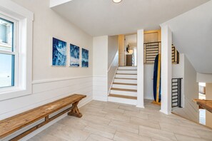 A spacious interior with a wooden bench, a staircase, and a view through an open door.