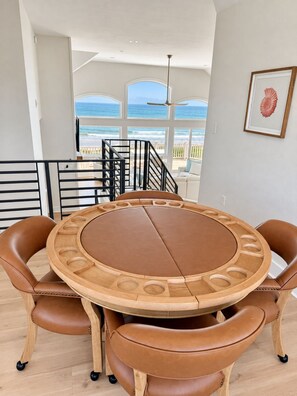 Et rundt træbord med læderstole, havudsigt gennem store vinduer og en trappe op til en balkon.