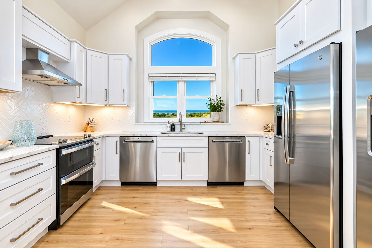 A modern kitchen with white cabinetry, stainless steel appliances, and a view through a window.