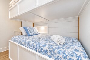 Un lit superposĂ© avec une tĂȘte de lit blanche, une table de chevet avec une lampe et une couvre-lit Ă motifs floraux bleus.