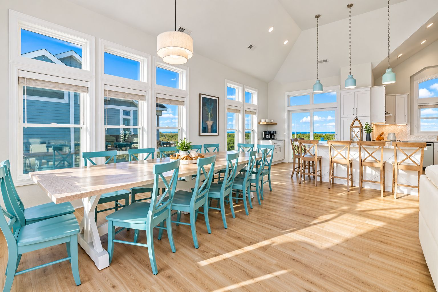 A spacious kitchen with large windows, a dining area with teal chairs, and a view of the outdoors.