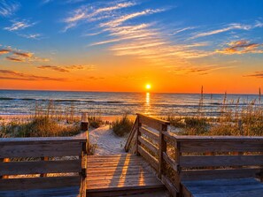 A wooden boardwalk leading to a beach with the sun setting over the ocean. - 🌊 Salty Treat | Luxury Oceanfront | Private Heated Pool⛱️Hot Tub & Ocean Views (Corolla)