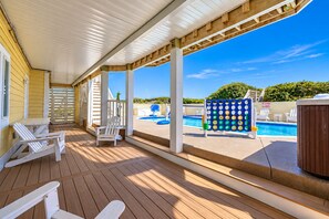 Una terraza techada con piso de madera, sillas blancas y un área de piscina con letrero de prohibición de clavados.