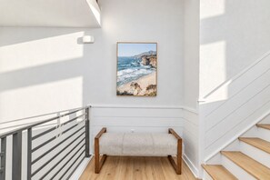 A staircase with a bench, a framed picture of a coastal landscape, and a white wall. - 🌊 Ultra-Luxury OCEANFRONT | Private Heated Pool🏖️Hot Tub & Unmatched Views! (Corolla)