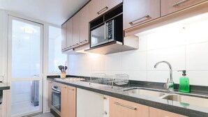 A modern kitchen with a built-in microwave, a stainless steel sink, and wooden cabinets. - Upper Views 2D Wifi, Balcony & Parking (Las Condes)