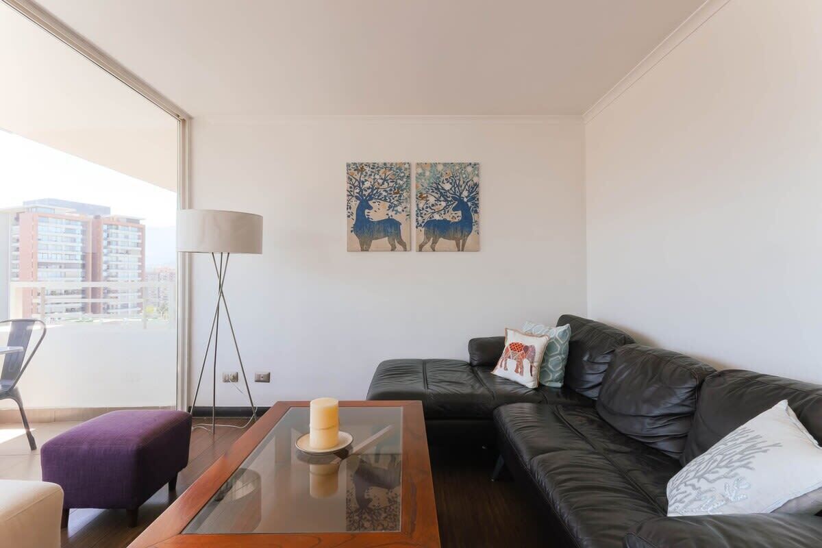 Een moderne woonkamer met een glazen salontafel, een zwarte leren bank en twee aan de muur hangende schilderijen van herten.