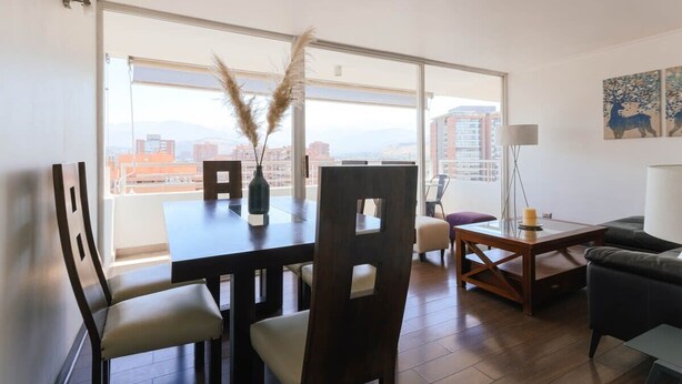 A modern living room with a dining area, large windows, and a city view. - Upper Views 2D Wifi, Balcony & Parking (Las Condes)