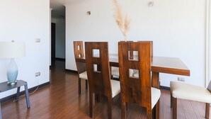 A dining area with a wooden table and chairs, a lamp on a side table, and a decorative plant. - Upper Views 2D Wifi, Balcony & Parking (Las Condes)