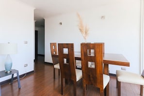 Zona pranzo con tavolo e sedie in legno, una lampada su un tavolino laterale e una pianta decorativa.