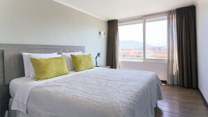 A hotel room with a large bed, a view of the city, and a window with curtains. - Upper Views 2D Wifi, Balcony & Parking (Las Condes)