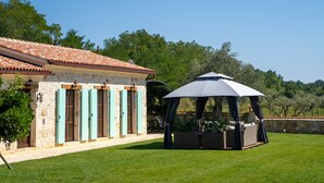 Un bâtiment en pierre avec un toit en tuiles, un espace extérieur abrité avec des sièges et une pelouse bien entretenue.