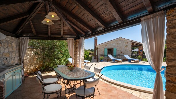 Un espace extérieur abrité comprenant une piscine, des murs en pierre et une table à manger avec des chaises.