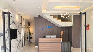A modern reception area with a marble wall, a wooden reception desk, and a staircase with a unique design.