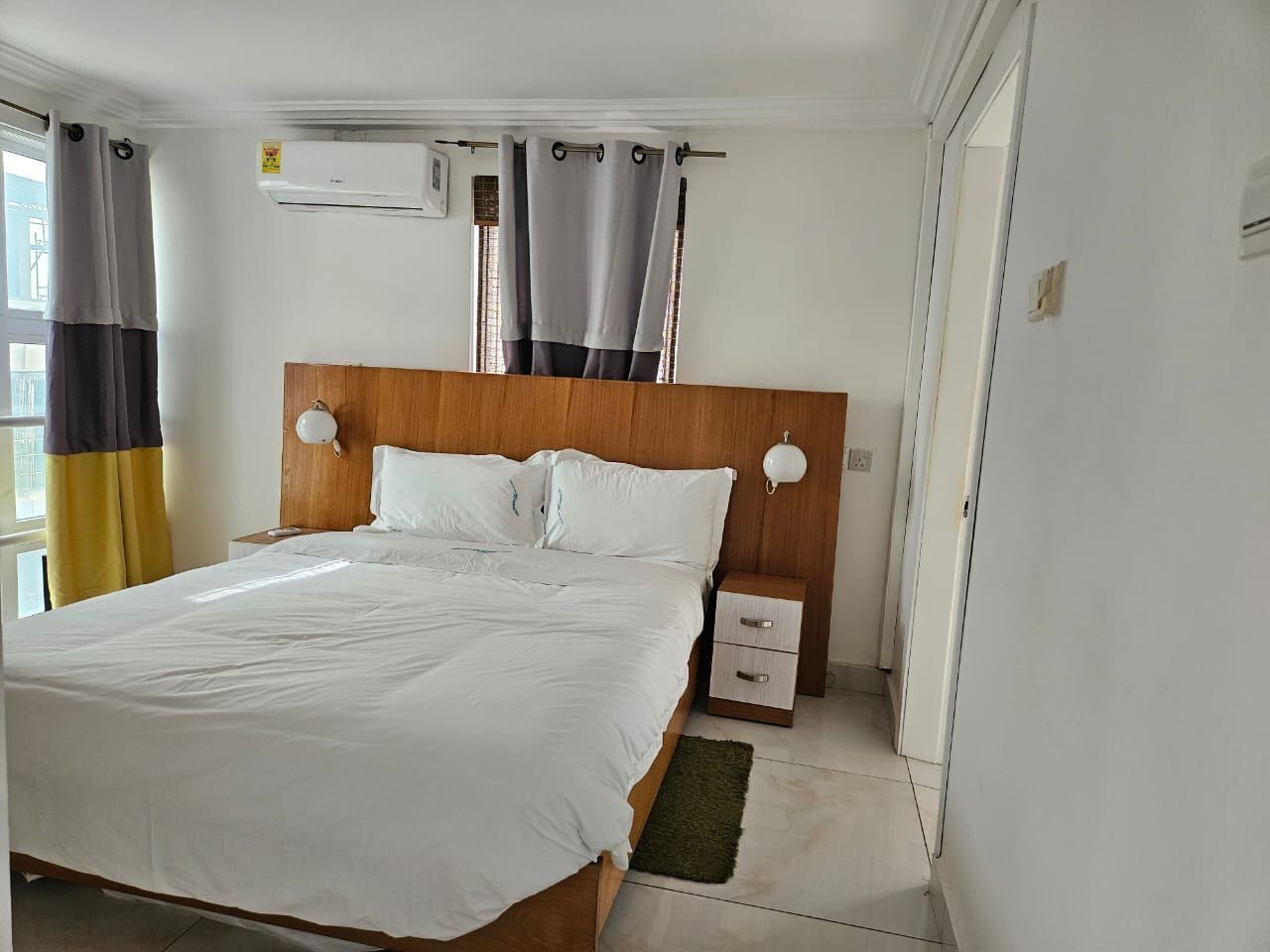 A bedroom with a wooden headboard, a single bed, a bedside table with drawers, and a nightstand with a lamp.