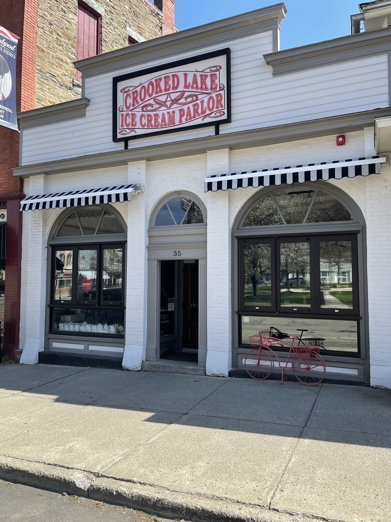 A building with a sign reading "Crooked Lake Ice Cream Parlour" and a bicycle parked outside.