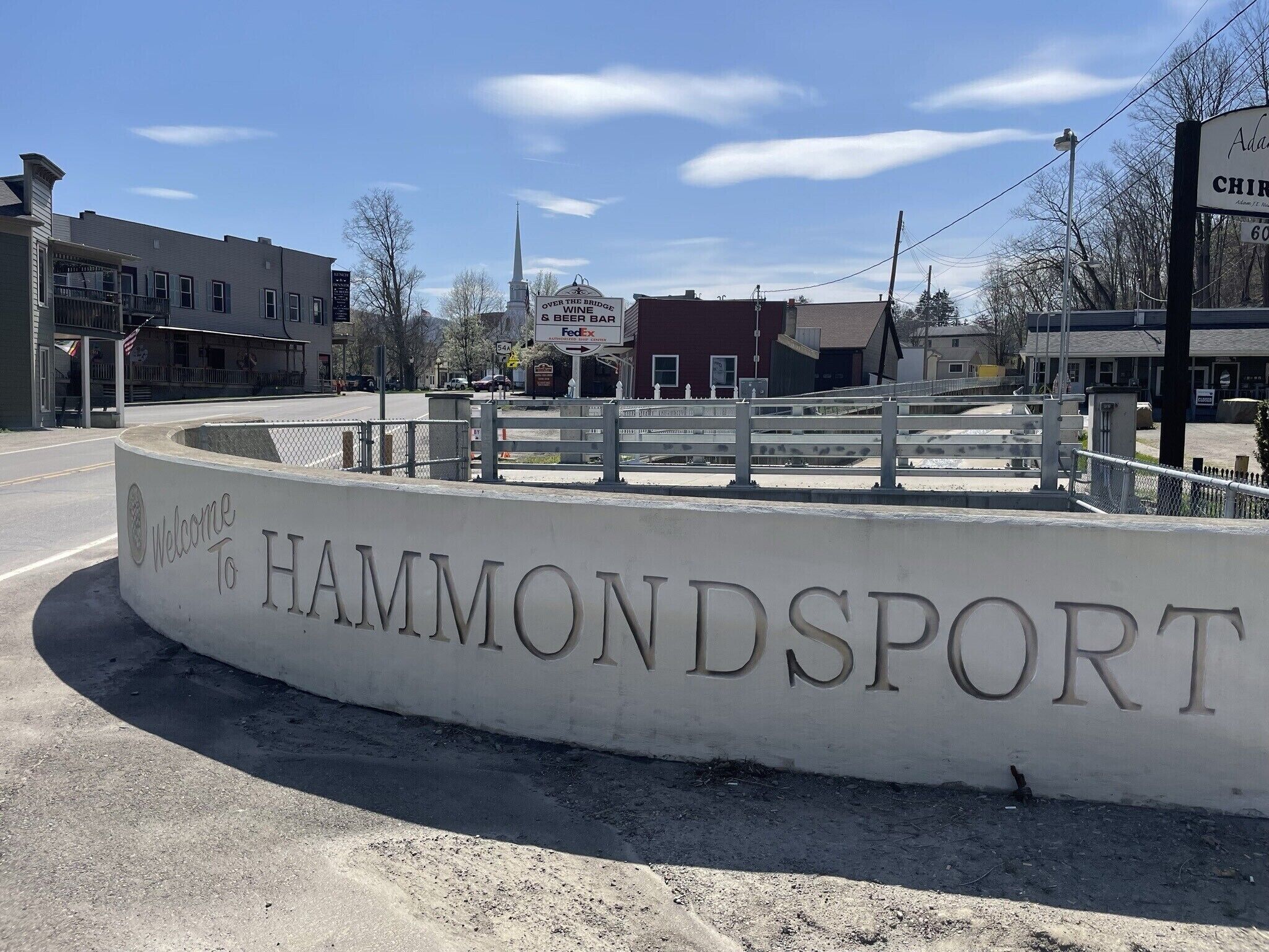 A welcome sign for HammondSport with a clear road and buildings in the background.