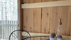 A glass table with two chairs, a book, and two thermoses on a wooden deck with a wooden wall in the background. - HARVEST MOON - ROMANTIC - OFF GRID - WINE TRAIL CABIN - Pet Friendly! 4 Seasons (Prattsburgh)