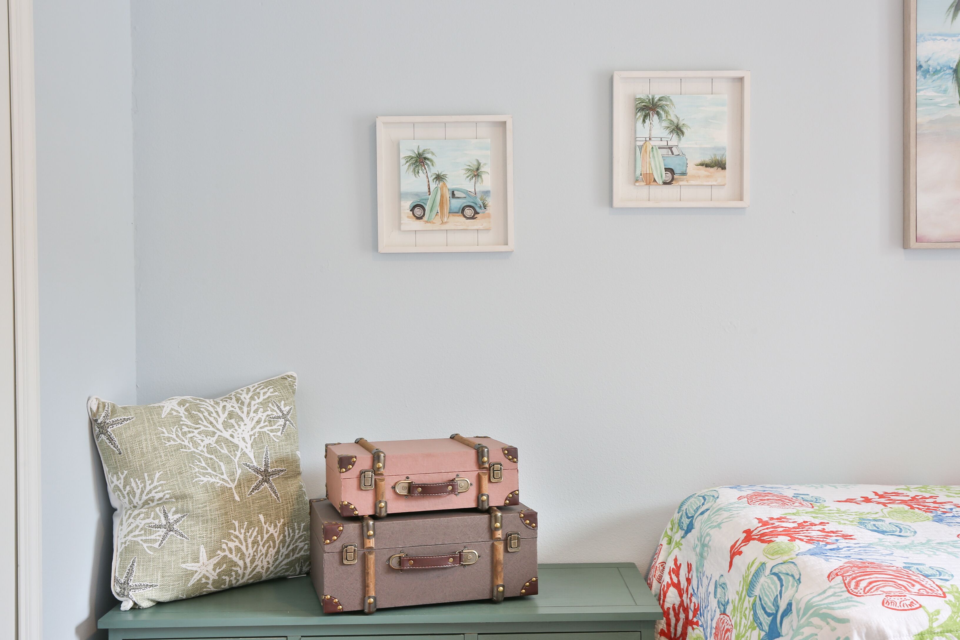 A room with a bed, a bench with suitcases, and two framed pictures on the wall.