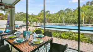 Un área de comedor al aire libre con vistas a una piscina y abundante vegetación.