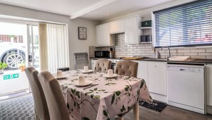 A dining area with a table set for four, a kitchen with white cabinets and a microwave, and a window with blinds. - Rock Hollow (Halifax)