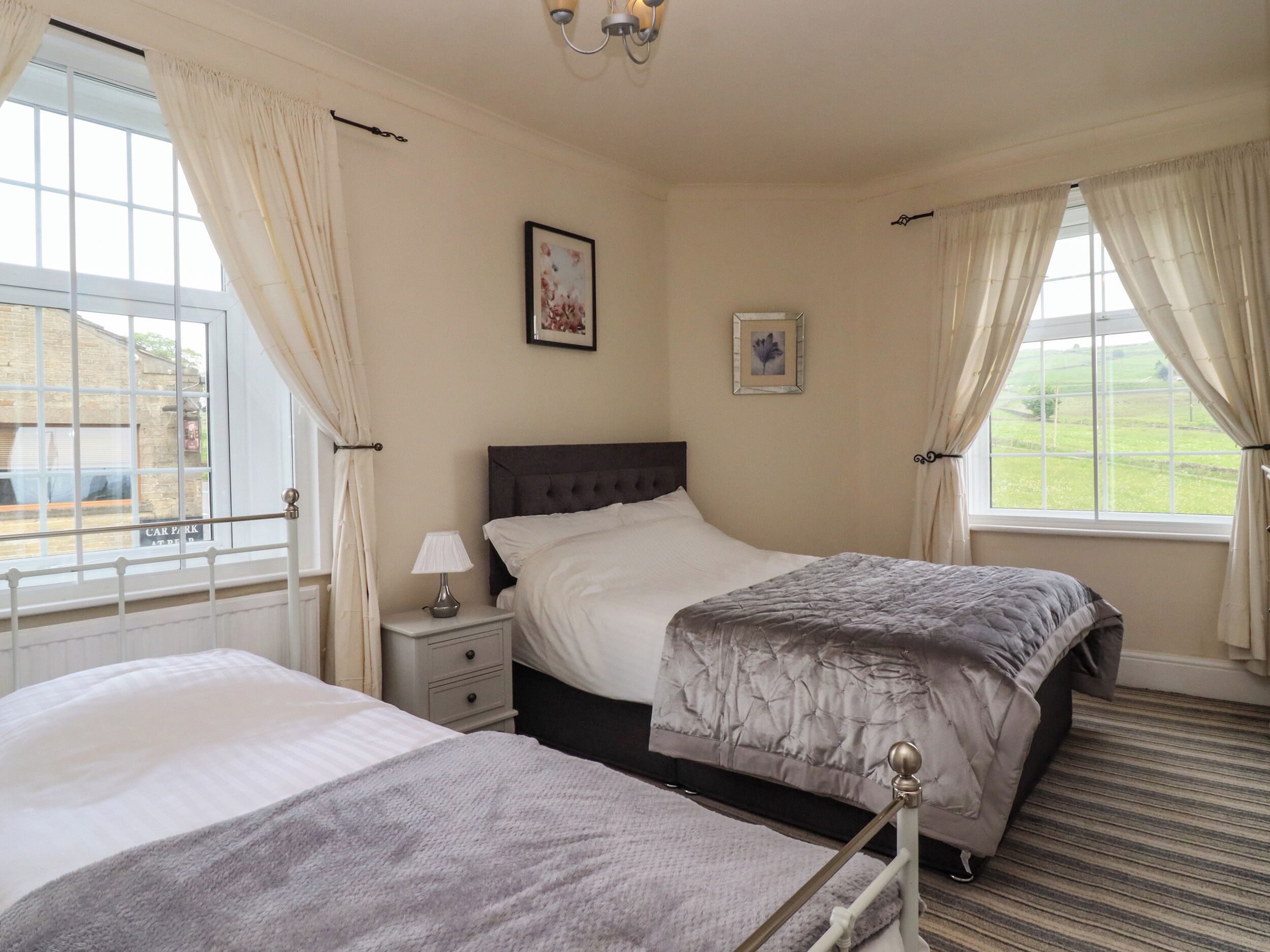 A bedroom with two beds, a nightstand, a lamp, and a window with curtains.