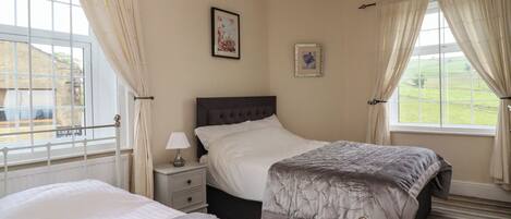 A bedroom with two beds, a nightstand, a lamp, and a window with curtains.