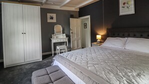 A bedroom with a large bed, a vanity with a mirror, a white wardrobe, and a nightstand with a lamp. - Rock Hollow (Halifax)