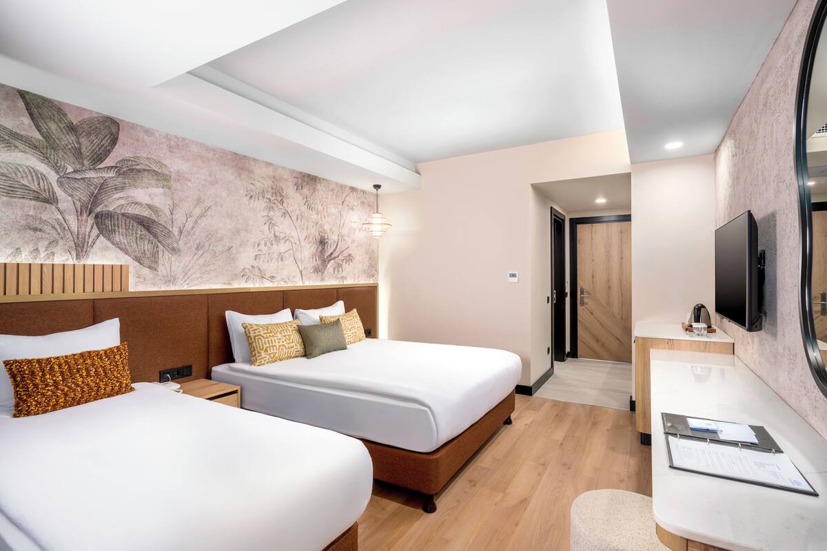 A hotel room with two beds, a desk, a television, and a large floral wall mural.