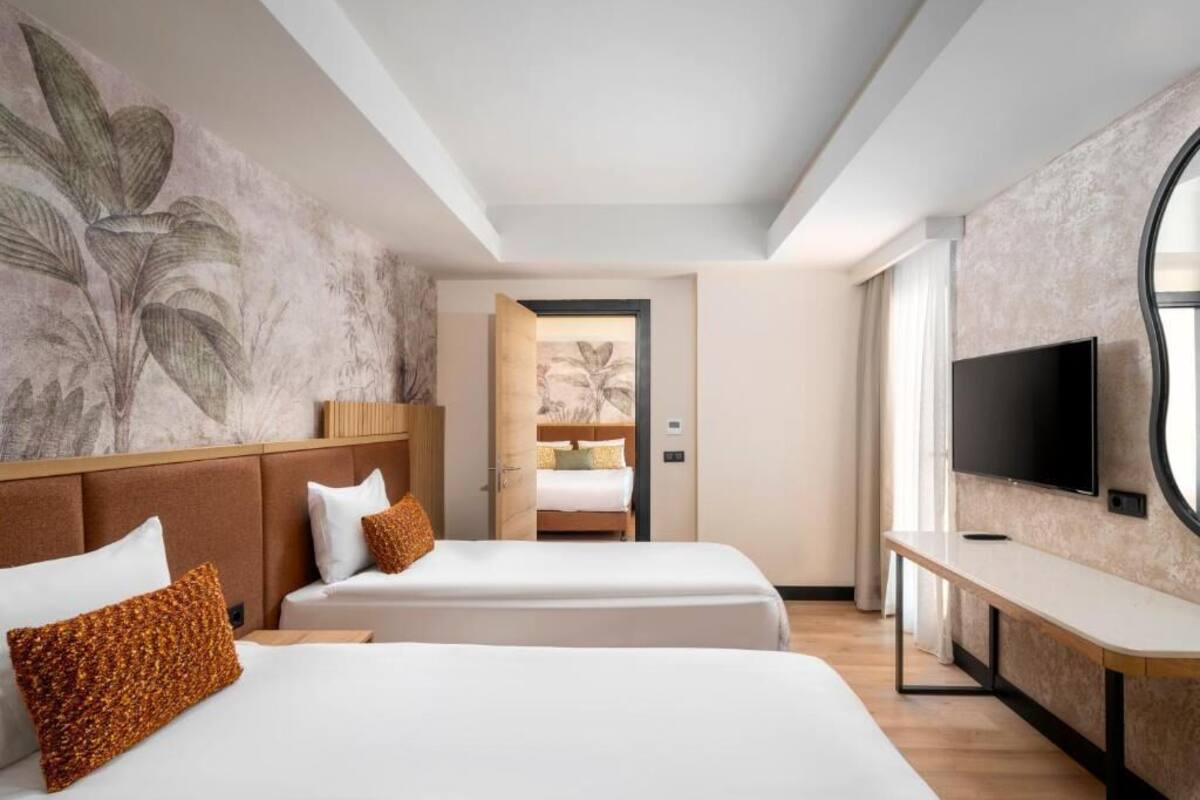 A hotel room with two beds, a TV, and a large window.