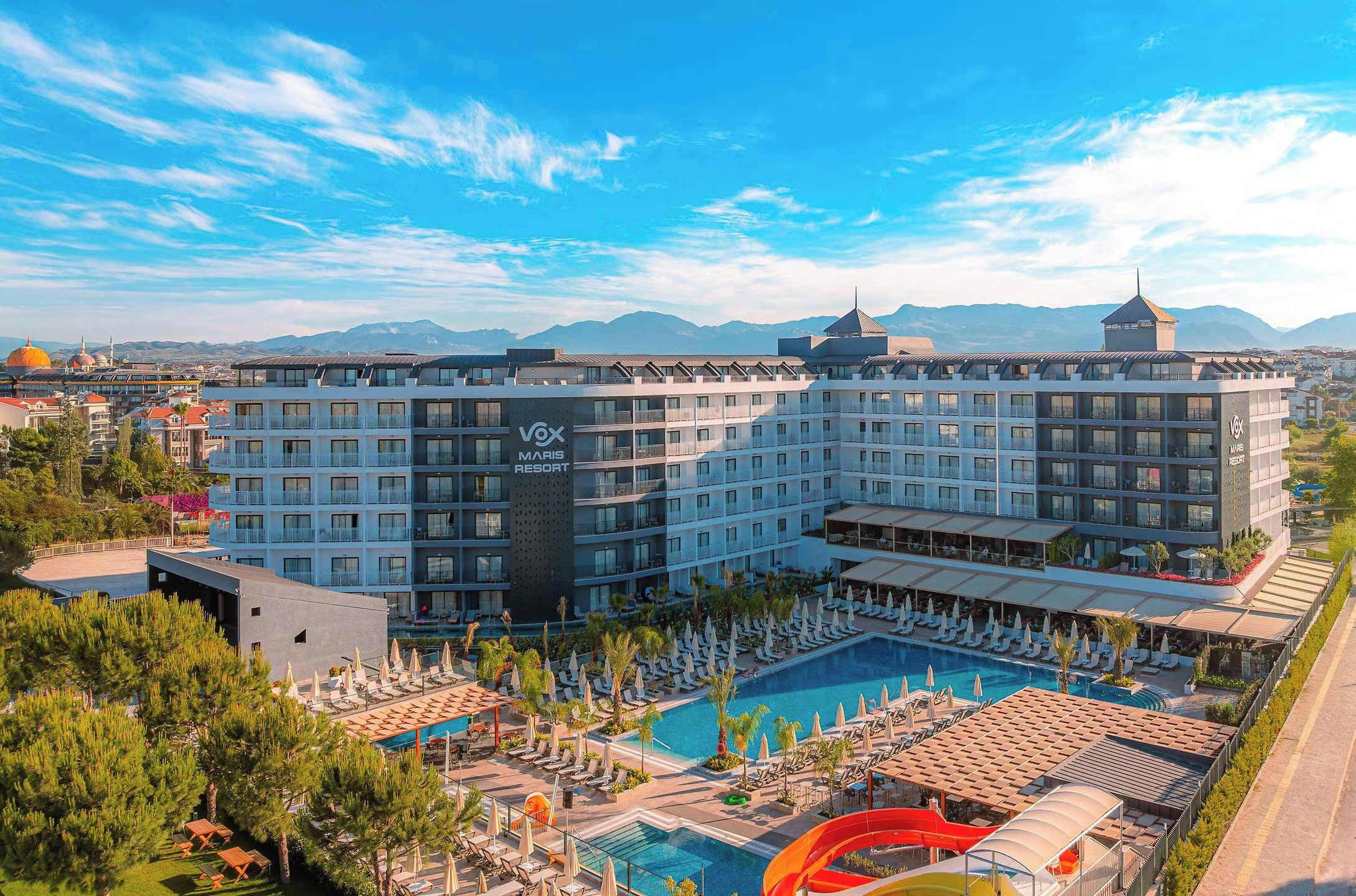 A hotel with multiple floors, a swimming pool, and a view of mountains in the background.