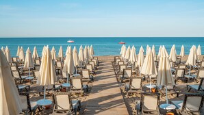 A beach with rows of sun loungers and umbrellas, a wooden walkway leading to the sea, and two boats in the water. - Vox Maris Resort- Ultra All Inclusive (Manavgat)