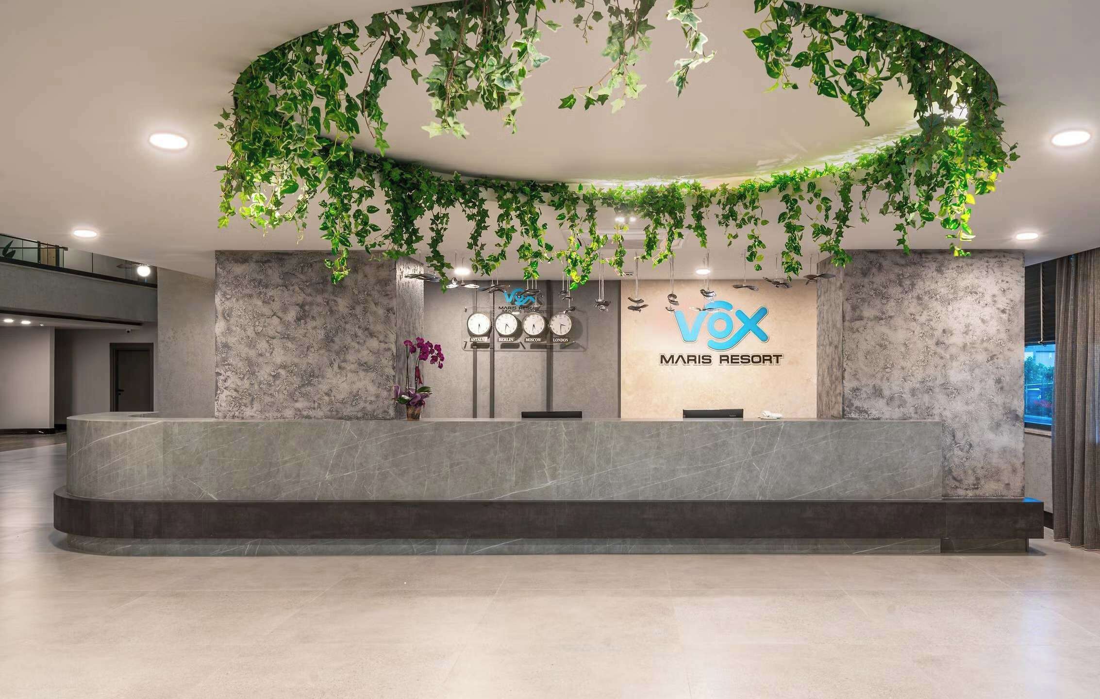 A reception area with a marble counter, a 'VOX MARIS RESORT' sign, and hanging greenery.