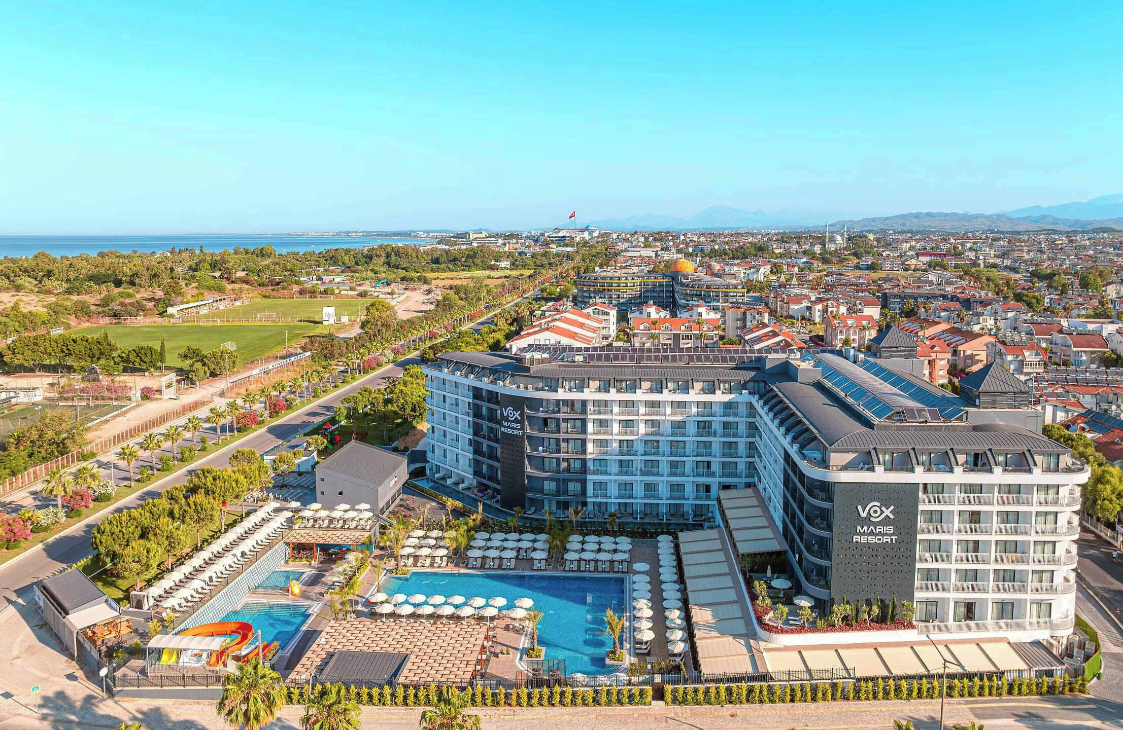 A hotel with multiple buildings, a swimming pool, and a view of the sea and mountains.