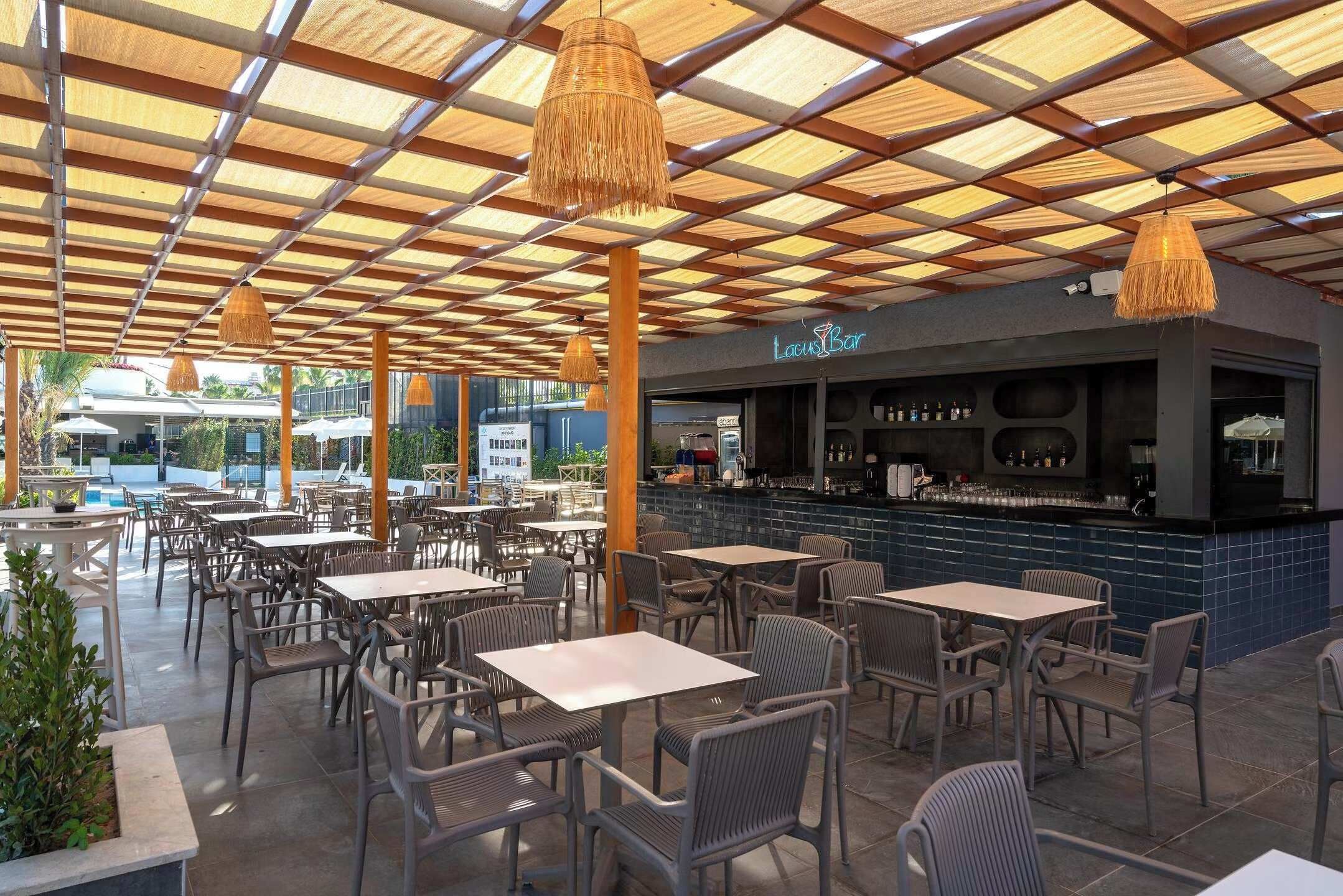 An outdoor seating area with tables and chairs, a bar, and a pool in the background.
