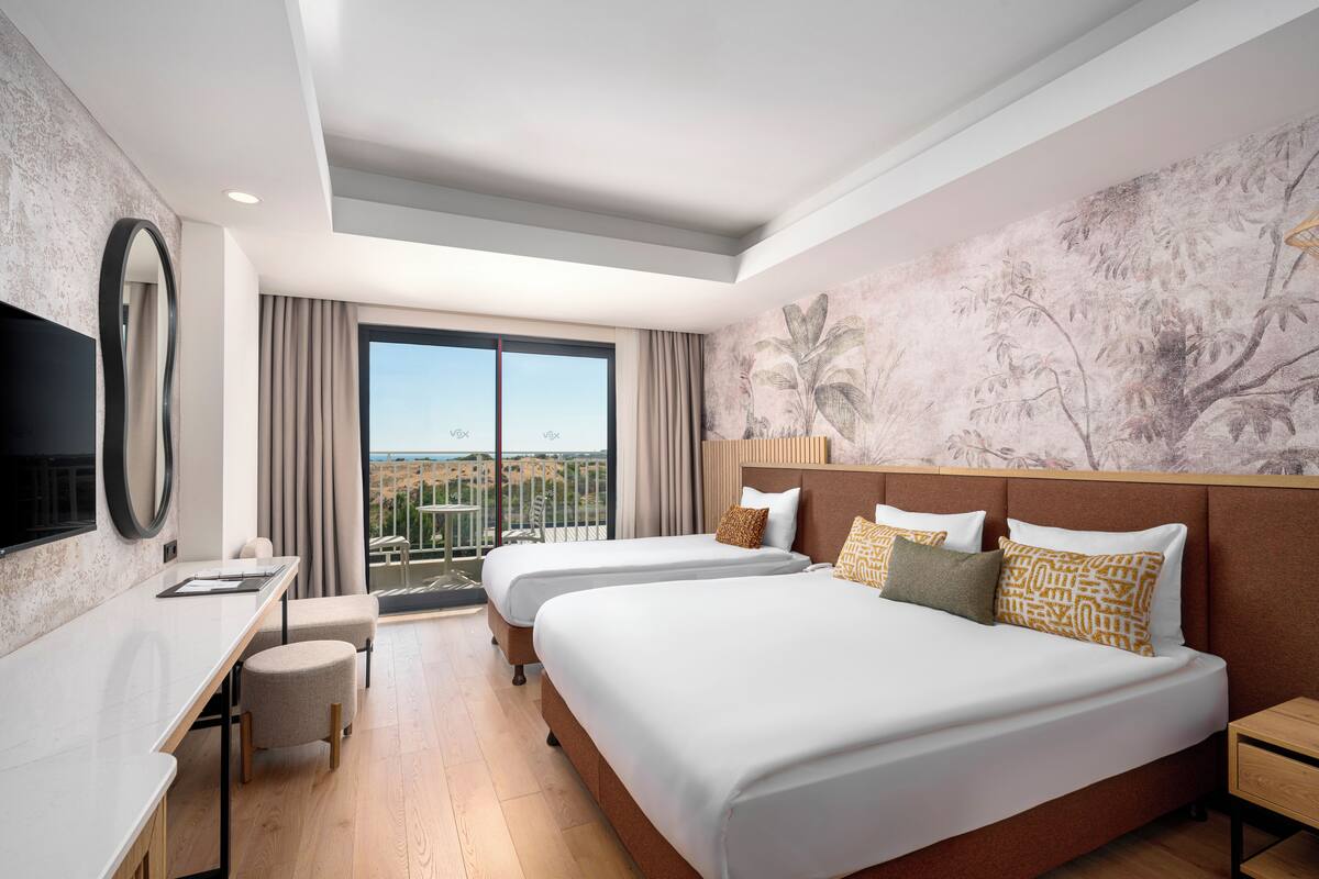 A hotel room with two beds, a desk, a chair, a TV, and a balcony with a view.