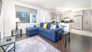 A modern living room with a sectional sofa, a glass coffee table, and a kitchen area with a refrigerator and microwave. - TownHome In Ottawa! (Ottawa)