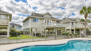 Un immeuble résidentiel doté d’une piscine, comprenant une structure à deux étages avec un balcon, une cour clôturée et un ciel d’un bleu éclatant.