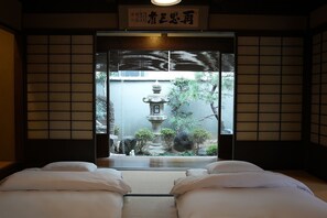 A traditional Japanese room with tatami flooring, a shoji screen, and a view of a garden with a stone lantern. - KAMIYASHIKI Private Hotel Self Check-in (Osaka)