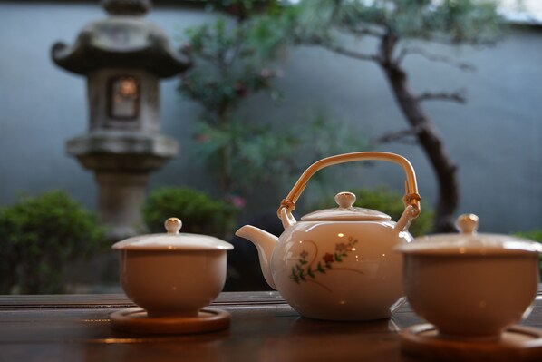 A traditional tea set with a teapot and two cups on a table, set against a backdrop of a stone lantern and greenery. - KAMIYASHIKI Private Hotel Self Check-in (Osaka)
