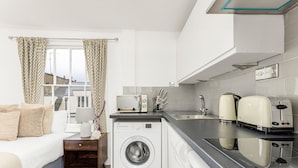A compact hotel room with a bed, a washing machine, a microwave, and a toaster. - The Paddington Rooms (London)